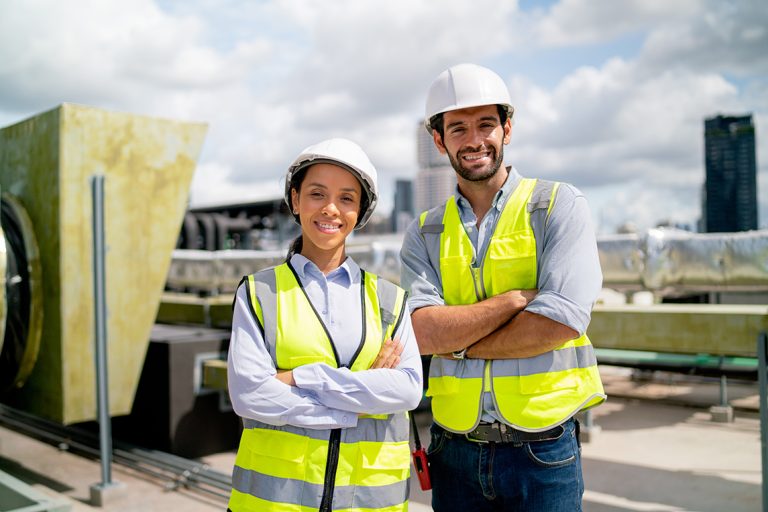 Two professional engineers smiling with arms crossed at a construction site, symbolising confidence, teamwork, and construction business coaching