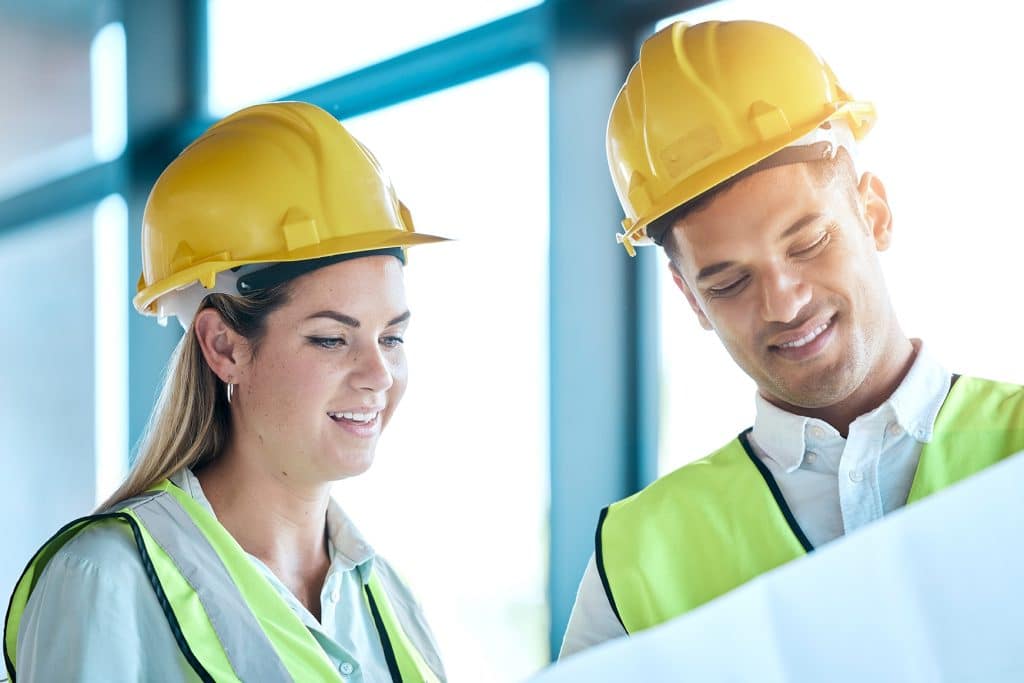 Architect and construction team smiling on-site with blueprints, engaged in planning and management training for construction success