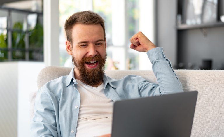 Young bearded man sitting on sofa at home using laptop computer, close up